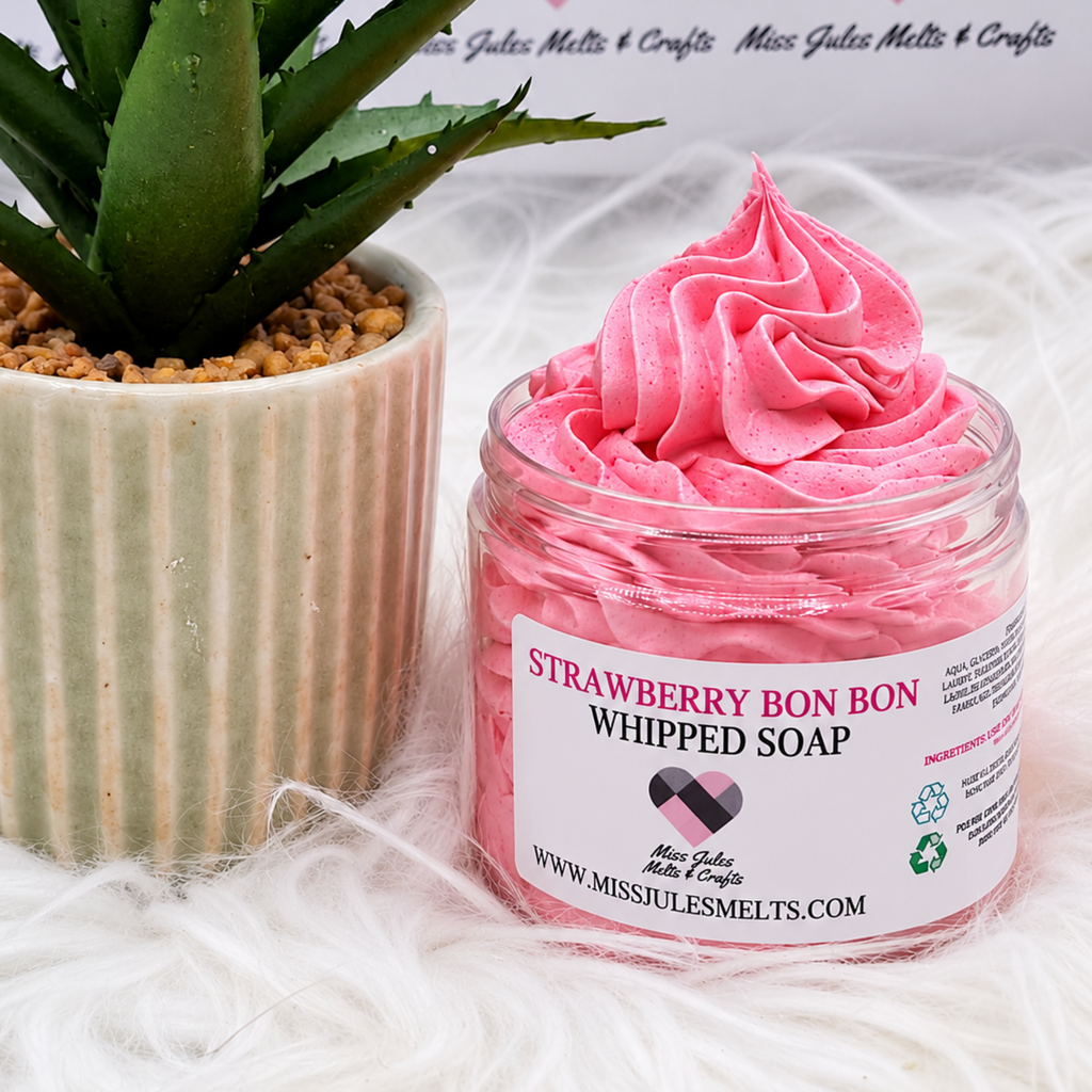 A jar of pink whipped soap labeled 'Strawberry Bon Bon Whipped Soap' by Miss Julia Melts & Crafts, styled next to a potted succulent on a white faux fur surface.